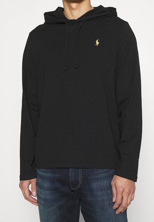 Black long-sleeve hoodie made of soft fabric, featuring a front pocket and a small gold emblem on the left chest. Drawstring hood detail.