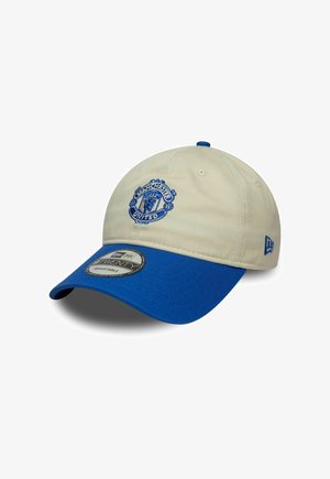 Manchester United baseball cap with beige crown and blue brim, adjustable strap, and embroidered team logo on front.