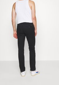 Svarta byxor med slim fit och subtila bakfickor, matchade med en vit linne och vita sneakers med blå detaljer.