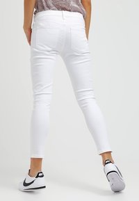 Bílé skinny džíny s hladkým povrchem; mají dvě zadní kapsy a středně vysoký pas. V páru s černobílými teniskami.