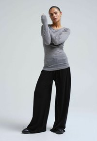 Grey long-sleeve top with fitted sleeves paired with loose black wide-leg pants. Textured fabric, relaxed fit, and flat black shoes.