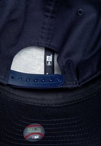 Cappellino da baseball blu scuro con tessuto texture, chiusura snapback regolabile e un adesivo del logo MLB rosso e bianco sulla parte interna.