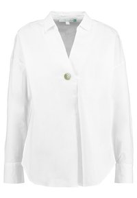 Weißes Langarmshirt mit V-Ausschnitt, das an der Vorderseite einen übergroßen grünen Knopf als Verschluss hat. Glattes, trockenes Material, lockere Passform.