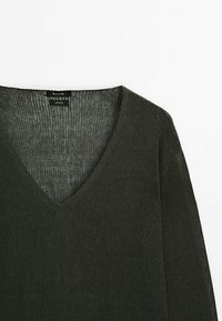 Ciemnozielony, luźny sweter z dekoltem w serek. Posiada teksturowany materiał oraz szerokie rękawy, eksponujące otwarty splot.