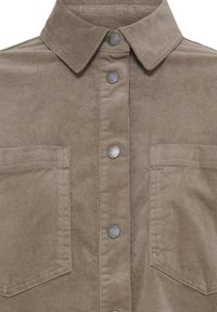 Chemise en velours côtelé marron avec un col pointu, des boutons-pression métalliques à l'avant et deux poches poitrine avec détails de couture.