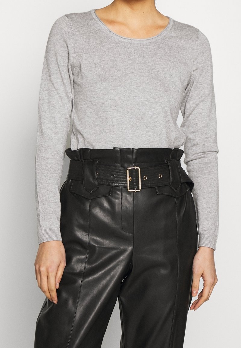 Top ajustado de manga larga en gris claro con escote redondeado, combinado con pantalones de cuero negros de cintura alta que presentan un detalle de cinturón con hebilla.