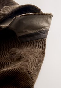 Tissu en velours côtelé marron avec une doublure intérieure lisse. Présente un accent gris foncé sur le col et une surface côtelée texturée.