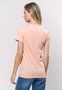 Pfirsichfarbenes Baumwoll-T-Shirt mit kurzen Ärmeln, rundem Ausschnitt, glatter Textur und regulärer Passform, von hinten vor neutralem Hintergrund gezeigt.