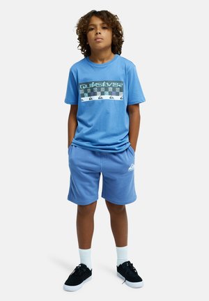 T-shirt bleu clair à manches courtes avec impression graphique ; short assorti bleu ; baskets noires ; chaussettes blanches montantes. Matière en coton doux, design décontracté.