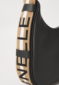 Borsa a tracolla nera in pelle con una cinghia intrecciata beige che presenta il testo "NELL" e una striscia bianca, tenuta da anelli in pelle nera su uno sfondo bianco.