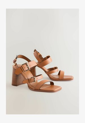 Bruine leren high-heeled sandalen met meerdere bandjes, goudkleurige hardwareaccenten en een schuine blokhak. Gladde textuur, open-tong ontwerp.