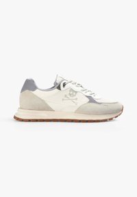 Zapatillas de ante en blanco y gris con un acabado texturizado, que presentan un logo de calavera y huesos cruzados, y una suela de goma marrón.