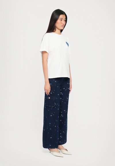 Valge T-särk sinise südame plaastriga, koos laia jala tumesiniste cargo pükstega, millel on tähe mustrid ja küljetasku. Elegantne terava ninaga jalats.