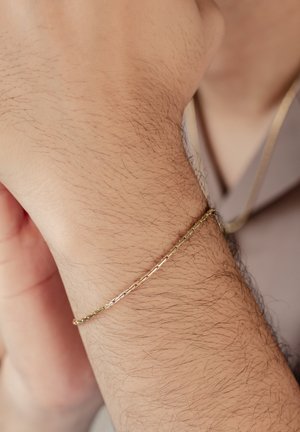 Goldfarbener Armreif mit einem gedrehten Design, der auf einem Handgelenk ruht. Die Oberfläche ist glatt mit einem dezenten Glanz und zeigt kunstvolle Details.
