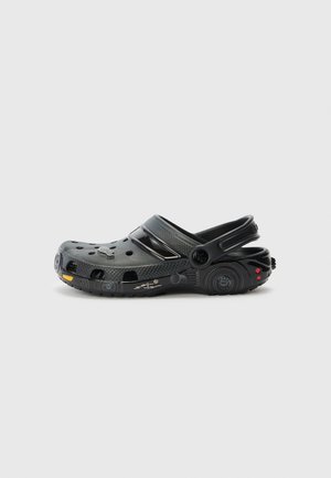 Sort clog-stil sko med ventilationshuller og en bagrem, med detaljerede designelementer, der ligner et køretøj på sålen og hælen.