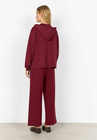 Sweat à capuche bordeaux avec une coupe décontractée, accompagné d'un pantalon large assorti en tissu doux. Accentué par une texture lisse.