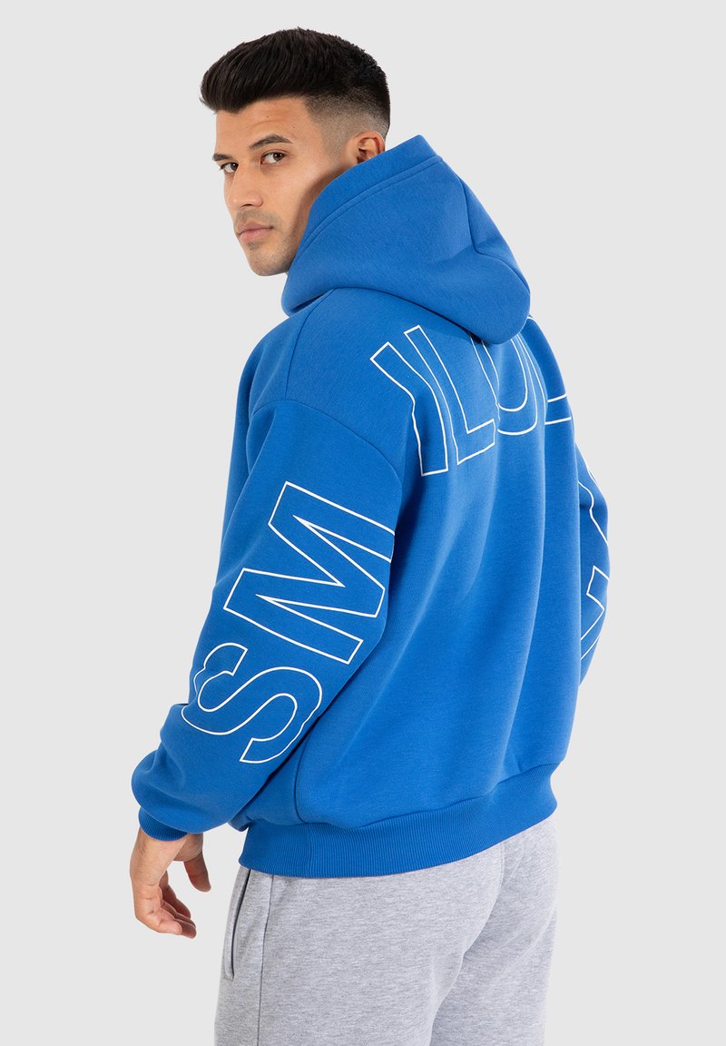 Blauwe hoodie van zachte stof, met een grote vozak en gedurfde witte tekst langs de mouwen. Comfortabele pasvorm met een trekkoord in de capuchon.