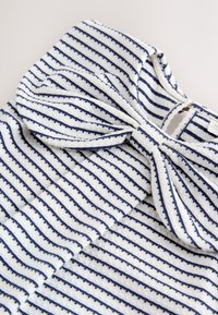 Tela blanca texturizada con rayas horizontales azul marino y un gran detalle de lazo atado en una prenda.