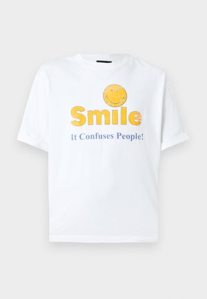 Bílé bavlněné tričko s krátkými rukávy s grafickým motivem žlutého smajlíka a textem „Smile It Confuses People!“ v modré barvě.