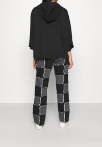 Överdimensionerad svart hoodie med en framficka, kombinerad med svart och grå byxor med lappar som har fransiga kanter. Vita sneakers.