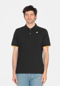 Polo nero con pattina a tre bottoni, logo bianco e maniche a righe con colori a contrasto in rosso e giallo. Materiale misto cotone.