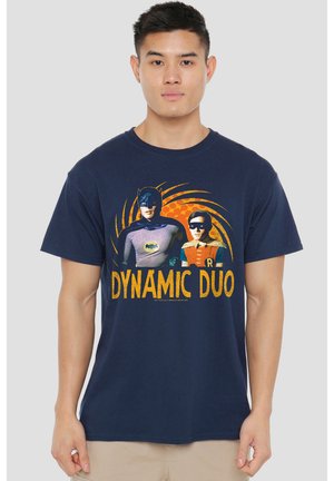 Mann, der ein dunkelblaues T-Shirt mit Batman- und Robin-Grafik und dem Text "Dynamic Duo" vorne trägt.