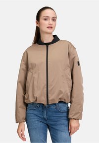 Giacca bomber color sabbia con colletto nero, zip frontale e tasche laterali. Presenta una texture liscia e una vestibilità rilassata.