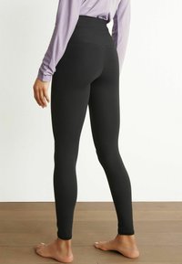 Leggings noirs taille haute en tissu extensible, design ajusté qui épouse les jambes, texture lisse et coupe à la cheville.