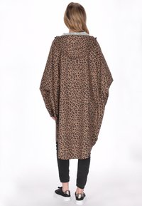 Barna és fekete színű leopárdmintás poncsó, kapucnis, bő szabású kialakítás. Fekete nadrággal és fémes részletekkel díszített tornacipőkkel párosítva.