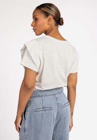 Lichtgrijze t-shirt met korte pofmouwen en verspreide zwarte spikkels, gecombineerd met hooggeknipte blauwe denim jeans met achterzakken.