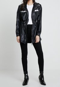 Černá nylonová bunda se zipem, stahovací pas a flitrové detaily na ramenech. Spárována s černými skinny džíny a lesklými kotníkovými botami.