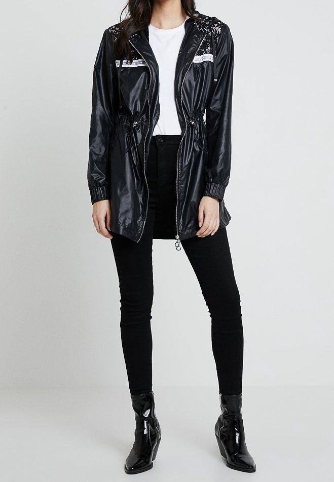 Černá nylonová bunda se zipem, stahovací pas a flitrové detaily na ramenech. Spárována s černými skinny džíny a lesklými kotníkovými botami.