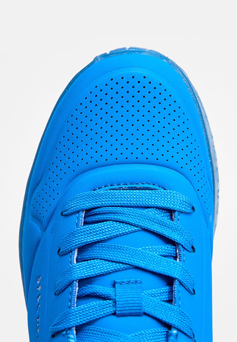 Scarpa sportiva blu con una parte superiore in sintetico liscio, punte perforate per la ventilazione e lacci piatti blu. Suola in gomma traslucida.