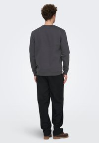 Grå sweatshirt med ribbede manchetter, klassisk rund halsudskæring og afslappet pasform, kombineret med sorte bukser og brune sko.