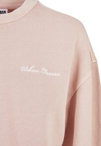 Felpa rosa chiaro con testo ricamato bianco "Urban Classics" sul petto, che mostra la parte superiore del torso e l'area delle spalle.