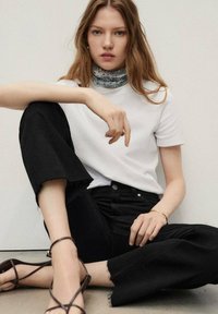 White fitted t-shirt, black wide-leg jeans with frayed hem, and brown strappy sandals. Blue patterned neck scarf adds detail.
