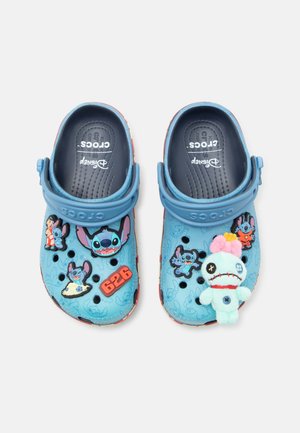 Blå Crocs sandaler med Disneys Stitch-karakter og andre relaterede vedhæng, inklusive en blød dukke og nummer 626 på venstre sko.