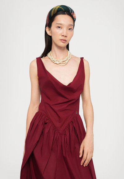 Burgundy dress with a deep V-neck and a draped bodice. Features a gathered skirt and a small logo accent. Paired with a patterned headband and pearl necklace.