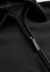 Sort fleecejakke med lynlås foran, tekstureret stof og en krave med blødt kantbånd. Indvendigt er der et mønstret foer.