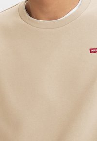 Beige sweatshirt med rund hals. Mjuk texur. Har en liten röd Levi's-logga på bröstet. Ren och enkel design.