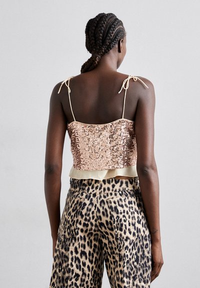 Top court en sequins rose doré avec des bretelles spaghetti, fini avec un ourlet volant léger beige. Porté avec un pantalon taille haute imprimé léopard.