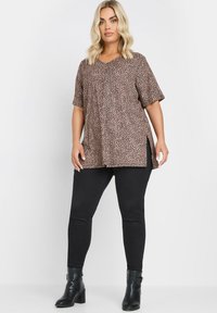 Blus med leopardmönster i lätt material med korta ärmar och sidofrackar, kombinerad med figursydda svarta jeans och svarta ankelstövlar.