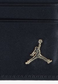 Sort læder kortholder med flere lommer, der har et fremtrædende guld Jumpman-logo. Glat tekstur med pæne syninger.