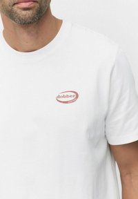 Hvid bomulds t-shirt med rund hals, der har et lille rødt "dobber" logo på venstre bryst. Korte ærmer, klassisk pasform.