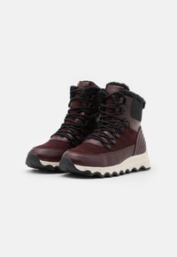 Scarponi da trekking color bordeaux con una combinazione di superfici lisce e testurizzate, design con lacci, colletto in pelliccia sintetica e suola in gomma bianca ondulata.