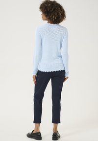 Hellblaues Strickpullover mit strukturiertem Muster, gesäumtem Saum, langen Ärmeln, kombiniert mit marineblauen Hosen und schwarzen Slipschuhen.