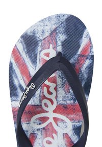 Flip-flop dengan sol bertekstur menampilkan desain Union Jack dalam warna merah, putih, dan biru. Strap karet hitam dengan aksen logo merek berwarna putih.