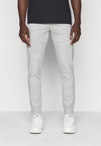 Grijze heather joggingsbroek gemaakt van zachte, rekbare stof. Aansluitende pasvorm met geribbelde boorden en zijzakken, gecombineerd met witte sneakers.