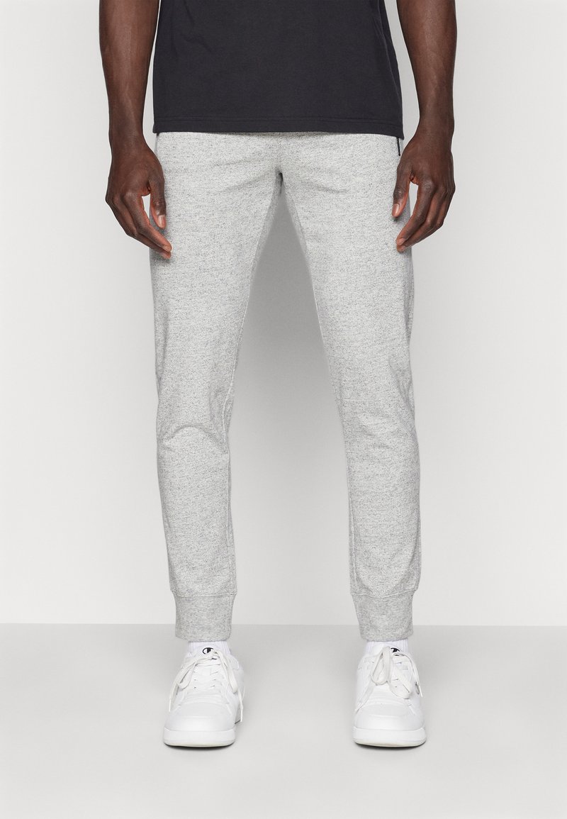Grijze heather joggingsbroek gemaakt van zachte, rekbare stof. Aansluitende pasvorm met geribbelde boorden en zijzakken, gecombineerd met witte sneakers.