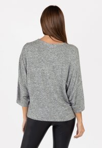 Maglione grigio a maglia con maniche a tre quarti e una vestibilità comoda. Texture morbida, collo rotondo e un sottile motivo mélange. Pantaloni neri aderenti.